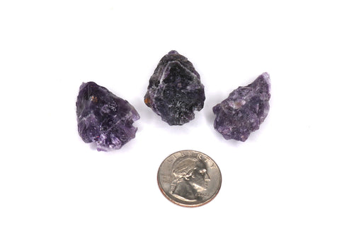 Three purple crystals with a quarter coin for scale on a white background