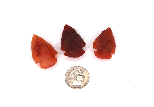 Three red arrowhead-shaped objects with a coin for scale on a white background
